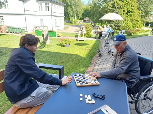 Seniore spēlē klavieres, bet pie galda tēja un sarunas ar brīvprātīgo